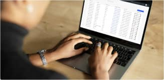 Man sitting on stool typing at a macbook