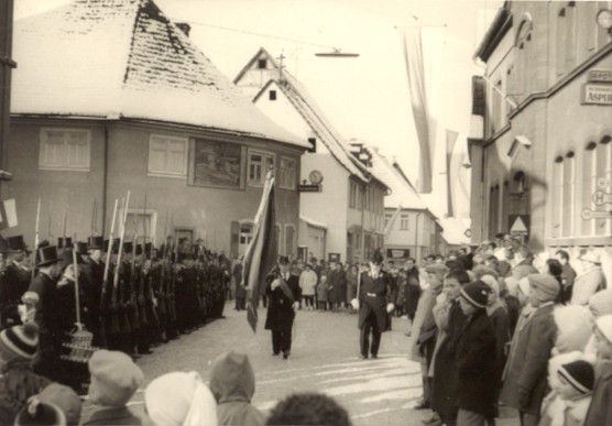Hauptmann Edmund Väth und den Fähnrich Georg Behl beim Fahne holen. Wie an der Uhr der Sparkasse zu sehen ist, ist es gerade 10:30 Uhr, also nach der Kirche am Morgen. Links im Bild sind Joseph Brönner, Kasper Spiegel und Wilhelm Hoffmann zu sehen.