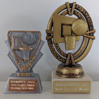 The Basketball Sussex League and Cup winners trophies that were awarded to each player in Worthing D&D. The league winner trophy is grey with a basketball about to go through the basket and is approximately 9cm in height. It is inscribed with 'BasketballSUSSEX 2021/22 Mens League Winner Worthing D&D White. The cup final winner trophy is gold painted and has a basketball about to go through the basket and is approximately 13cm in height. It is inscribed with 'BasketballSUSSEX 2022 Mens Cup Final Winner'.