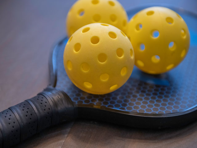 Three pickleball balls on top of a pickleball paddle
