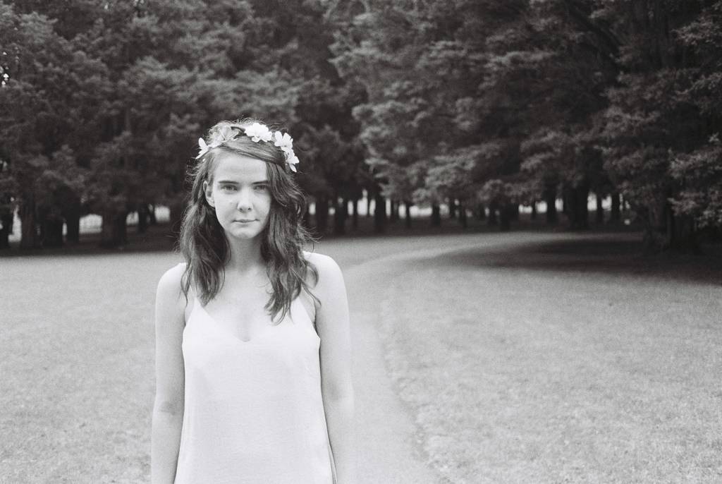 A woman standing in front of a path, trees and grass.