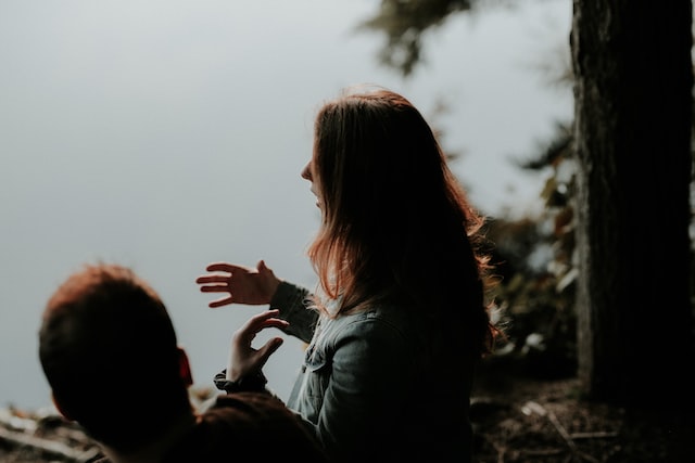 Person in blue jacket talking to a friend with hand gestures by a lake