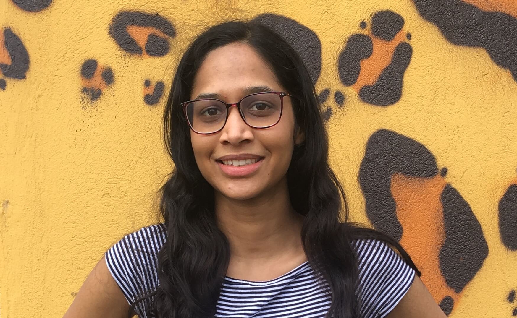 Sara Sinha smiling and posing in front of a wall.