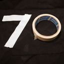Two short lengths of masking tape on black cloth forms a bold seven. The roll of tape rests alongside making the zero.