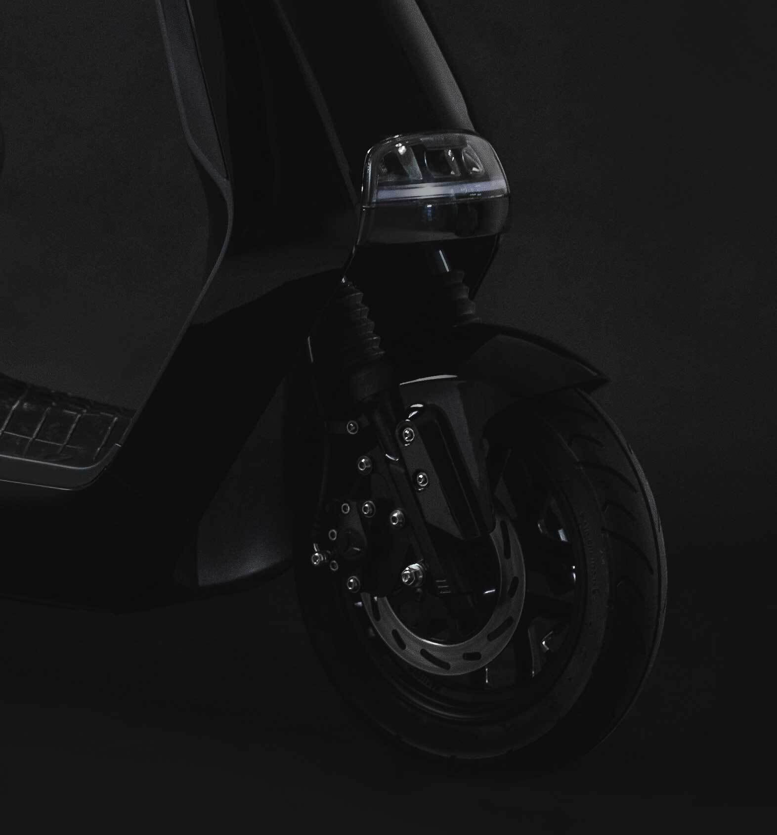 Dark image of the black Yadea e-moped zoomed in by the front wheel.