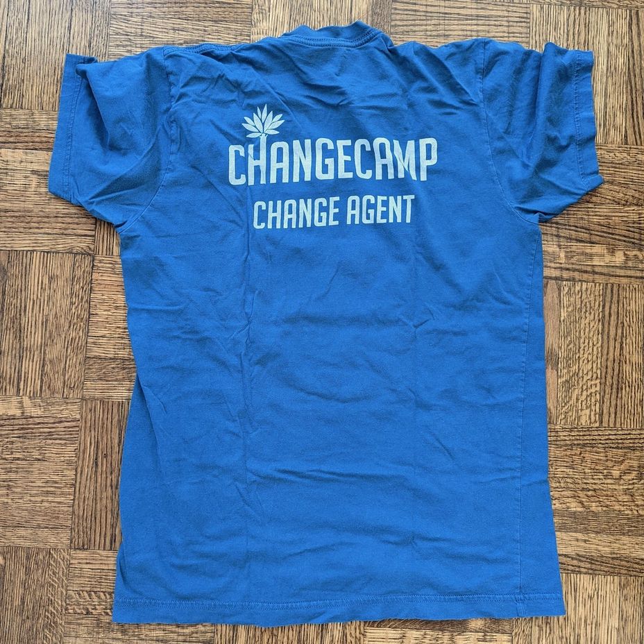 Back view of a blue T-shirt that reads “ChangeCamp Change Agent”
