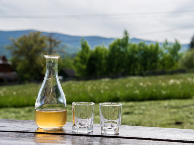 A bottle of Mead and two cups, laid out on a porch railing overlooking the mountains
