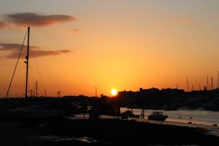 Sun setting behind the rooftops of Shoreham town. Silhouettes of small boats line the river in the foreground.