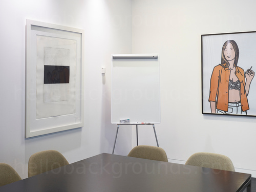 Basic meeting room featuring square black table with green fabric upholstered chairs next to white flip board and art piece  Zoom background