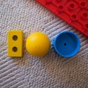 The number one hundred created from yellow and blue blocks and pieces from infant toys. A red Duplo base plate in on the biege rug alongside.