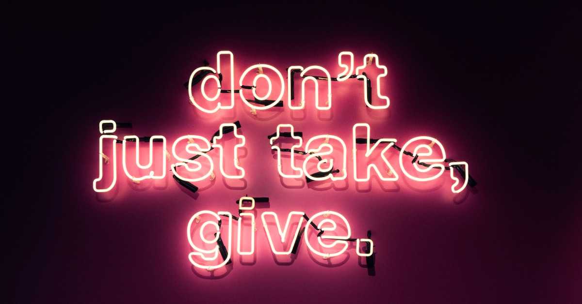 Der Schriftzug "Don't just take, give" in pinken Neonfarben auf dunklem Hintergrund