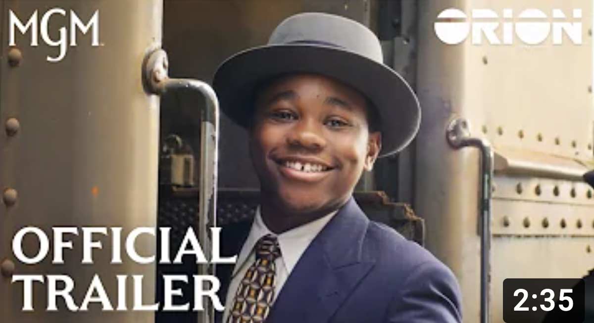 A thumbnail from the TILL film trailer showing Emmett Till wearing a suit and hat smiling and boarding a train.