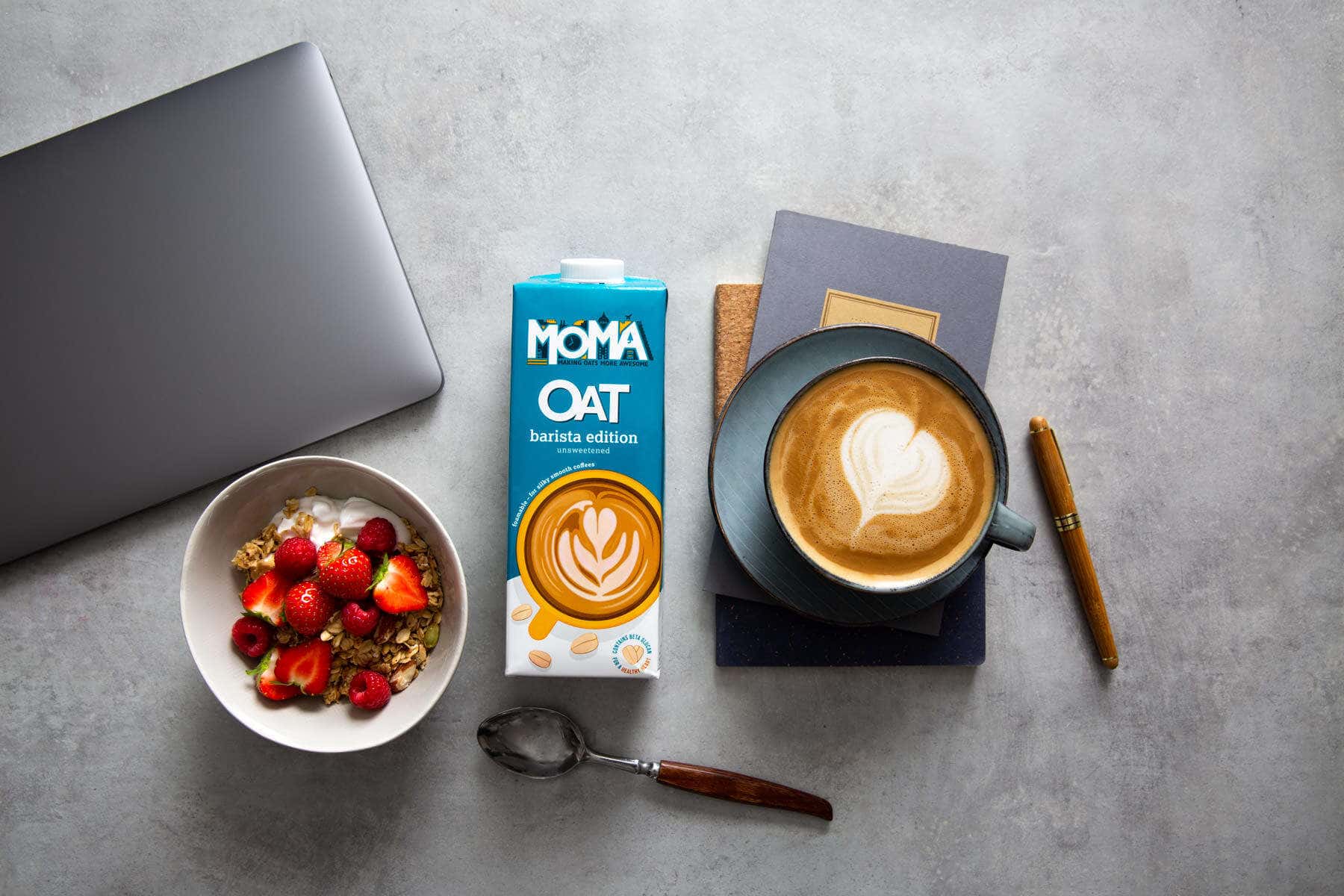 Oat milk carton with a coffee and muesli breakfast on a concrete top
