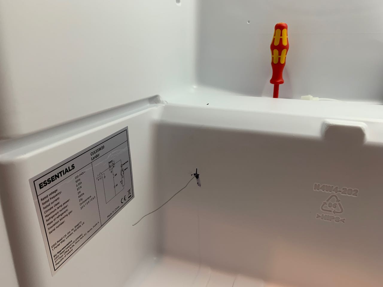 A photo showing the base of a fridge, with a pilot hole with wire
    coming through