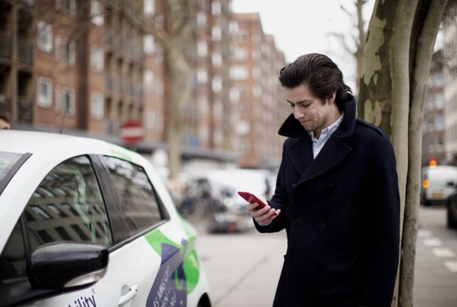 A caucasian male person holding a mobile device next to eCar.