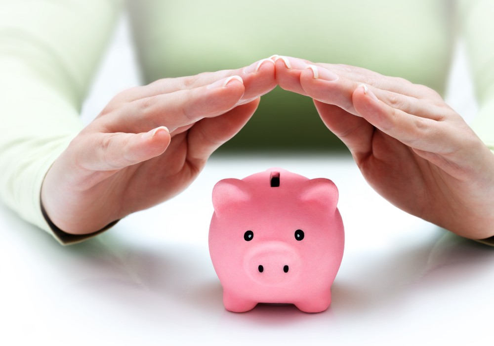Two hands covering a piggy bank to protect it