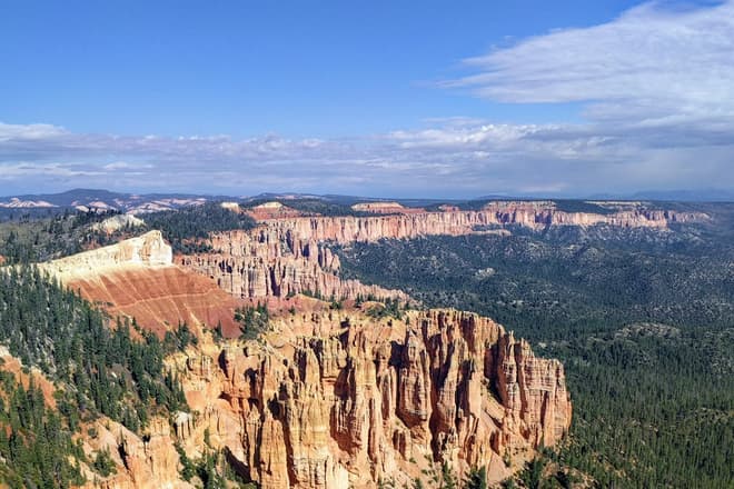The undulating South Wall of Bryce Canyon. Red and white pillars of soft rock cluster together, eventually becoming the rim of the Canyon. The pillars stop abruptly, and are immediately replaced by a pine forest.