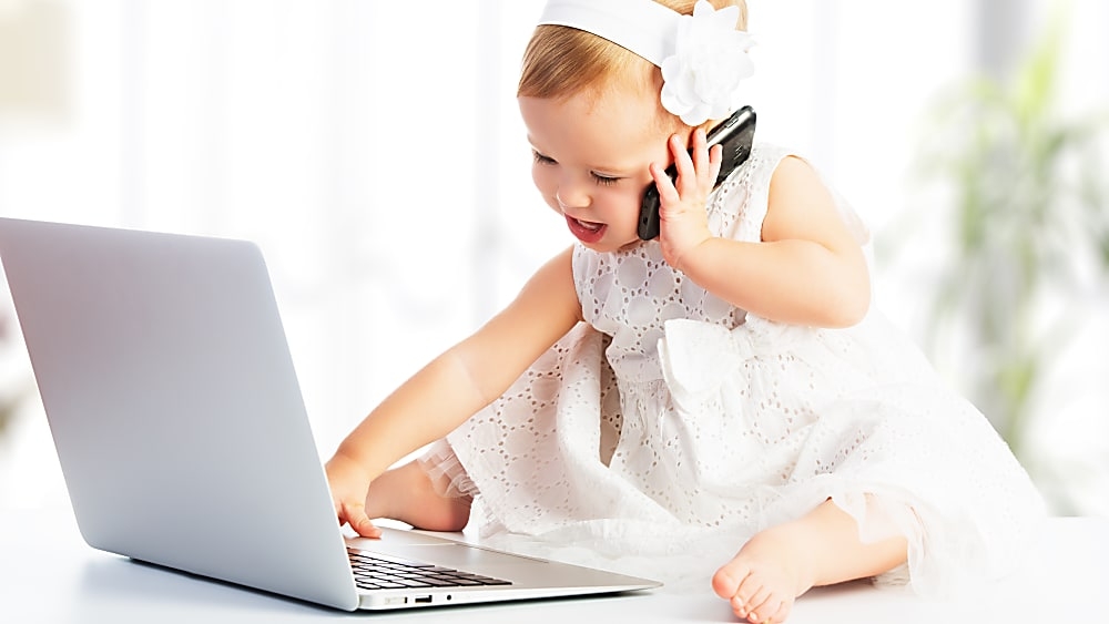 Baby girl talking on a phone in front of a laptop