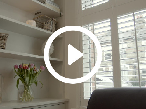 Sub-urban home interior presenting white shelves featuring trinkets and flowers next to window with street views Zoom background