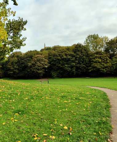Winding concrete path across Burley Village Green, surrounded by tall trees