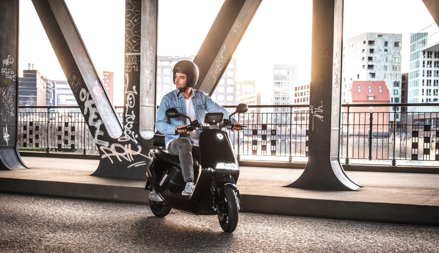 Wunder Vehicles Yadea moped with man riding on a bridge at sunset
