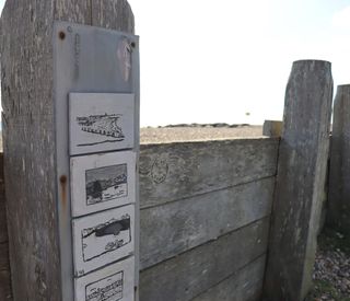 Four black and white ceramic postcards attached to a wooden post on the beach.