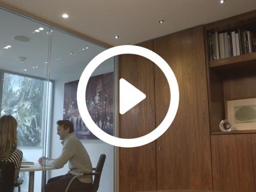 Partially glass walled office space containing wooden wall shelving and cupboard with view through to neighbouring room Microsoft Teams background
