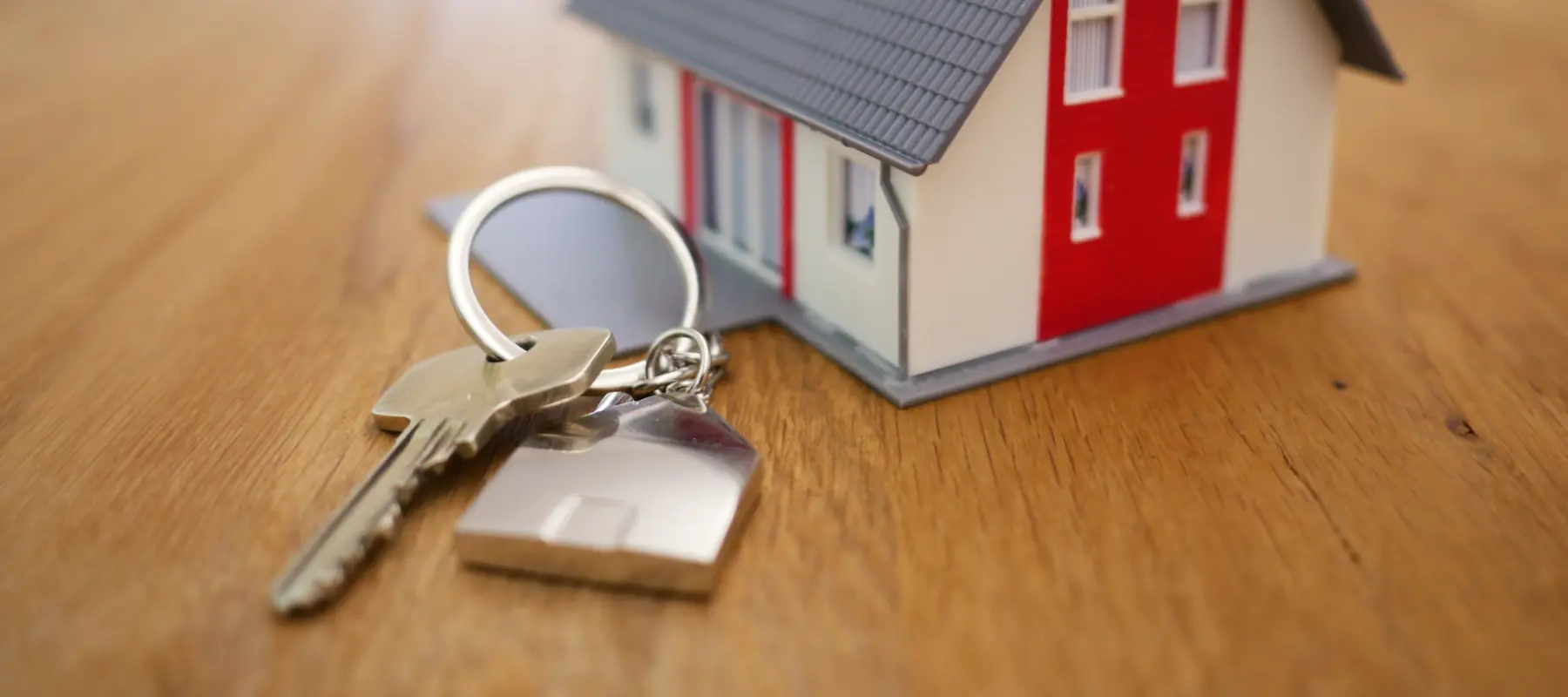 Uma chave de casa ao lado de uma maquete de uma casa sobre uma mesa de madeira