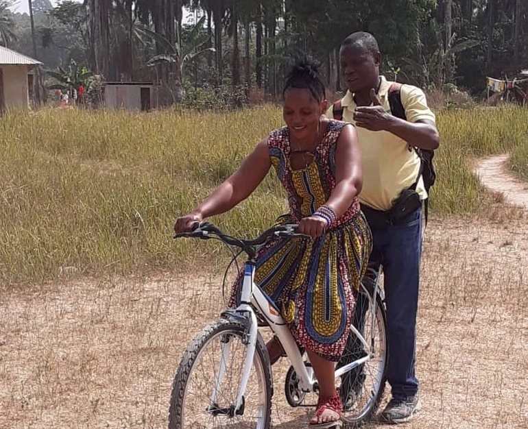 Woman riding a bicycle with a man standing behind her