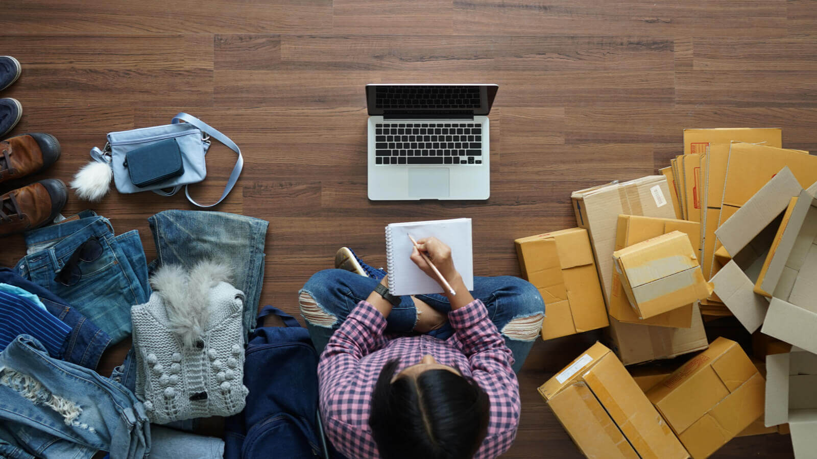 Person sitting in a living with clothes and boxes setting up an online Etsy store.