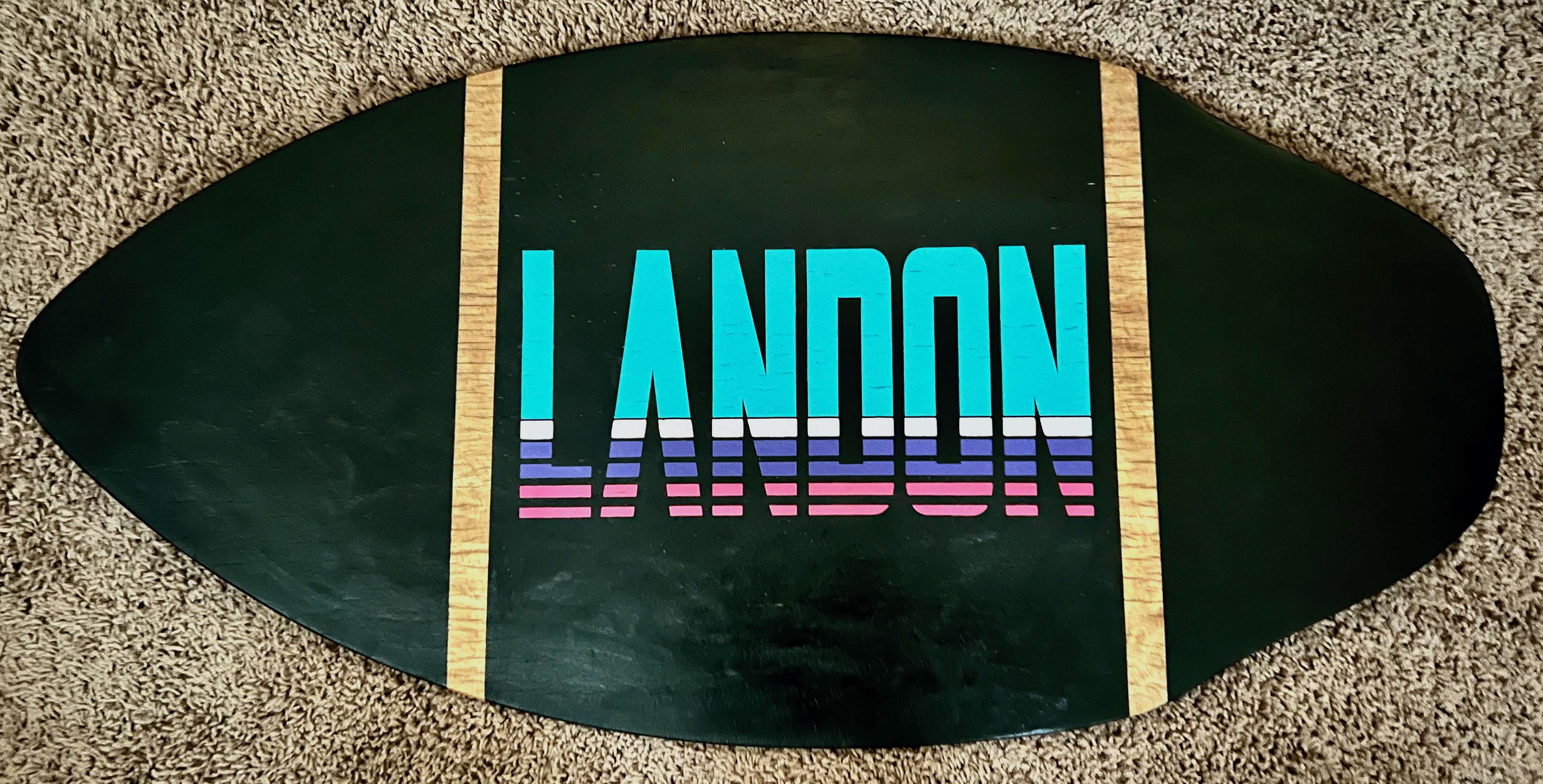 A photo of a skimboard with the name Landon painted on it.