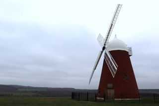 The red and white Halnaker Mill from a 45 degree angle. Surrounded by green grass and hills in the background.