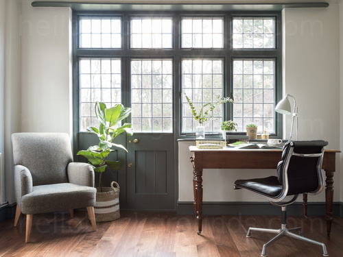 Calm private office with large windows and wooden flooring containing wooden desk with black chair next to grey armchair  Skype background