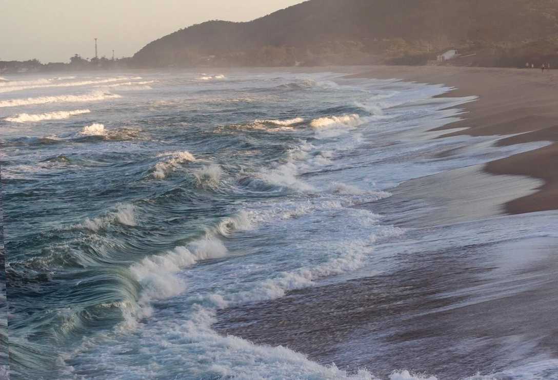 Ondas na areia a esquerda com faixa de areia a direita com vista da extensão da praia