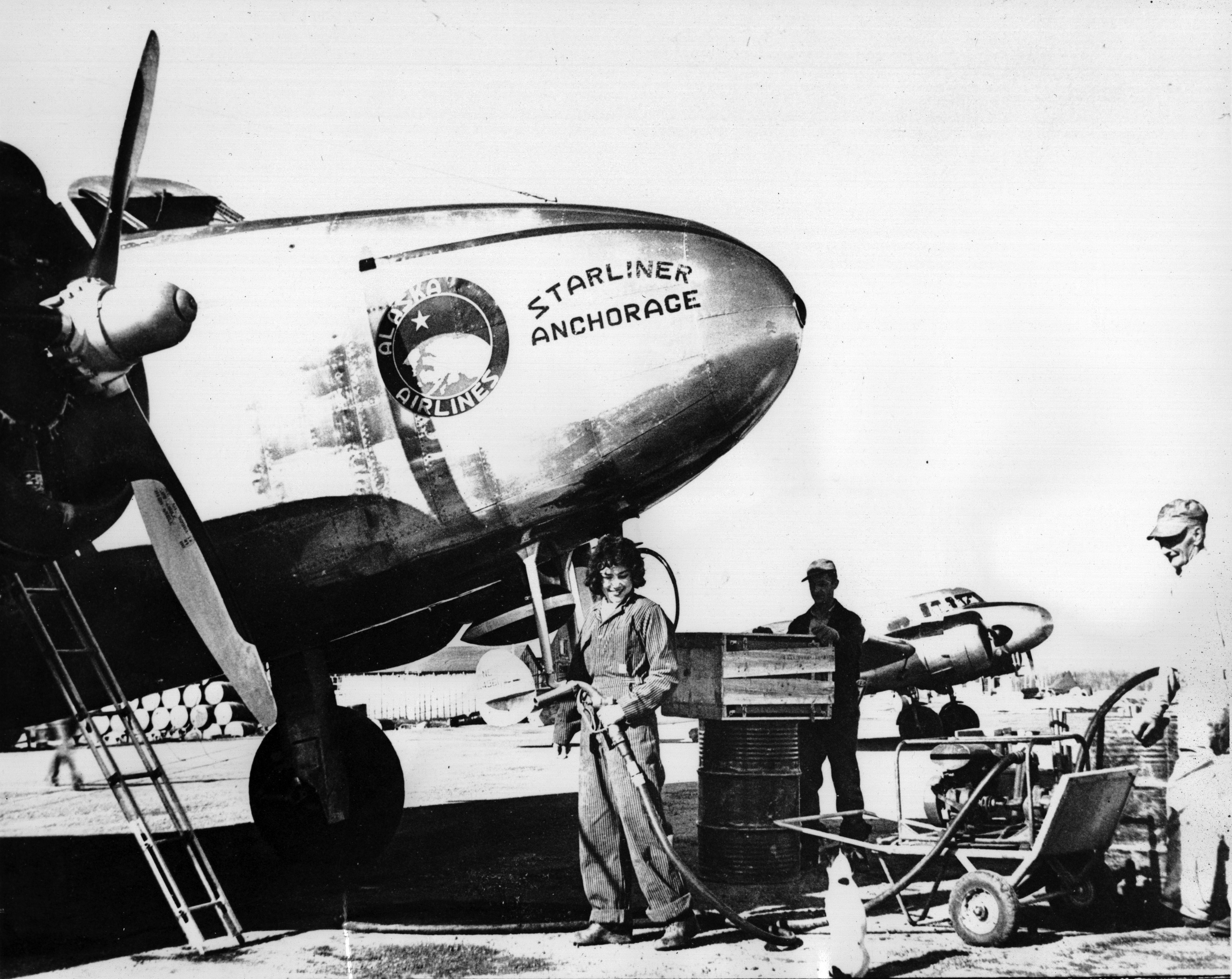 black and white photo of a young woman fueling a vintage airplane