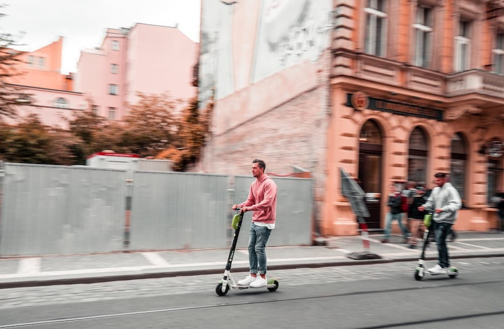 A caucasian man riding a kick-scooter on the street in the middle of an urban area.