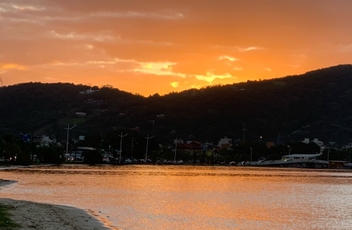 Por do sol com céu alaranjado por trás dos morros refletindo na água da lagoa