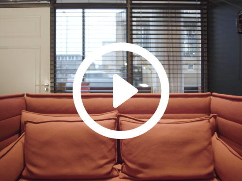 Intimate meeting room containing orange sofa in front of windows holding urban city view Zoom background