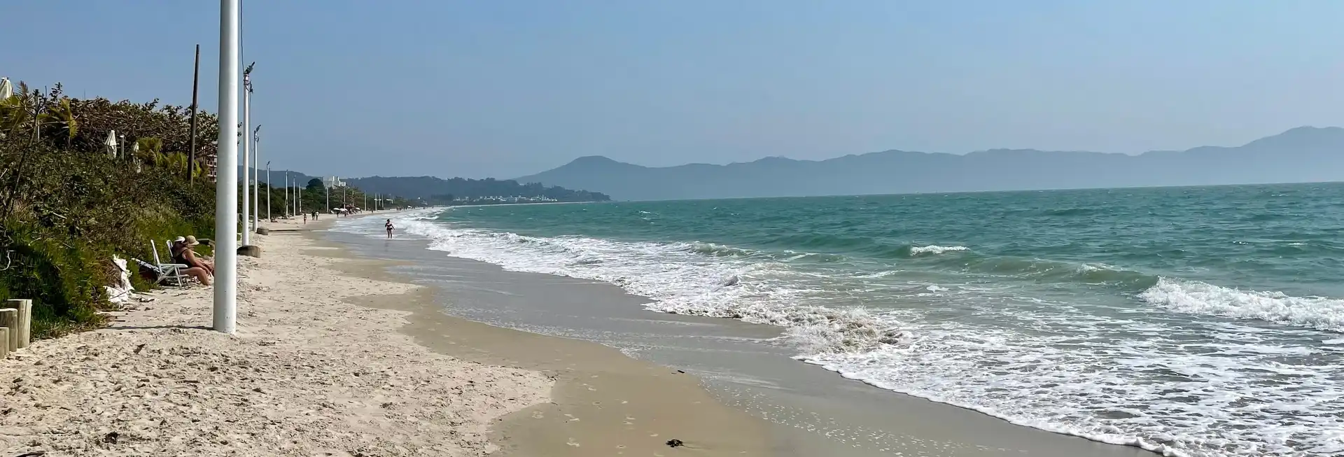 Vista da praia de Jurerê com curta faixa de areia a esquerda e mar a direita pegando até o horizonte