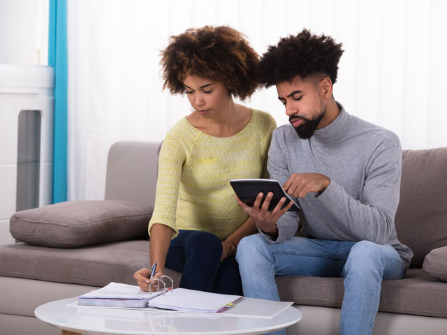 A couple sitting on their couch with a calculator and notebook, trying to create a budget for their checking and savings accounts