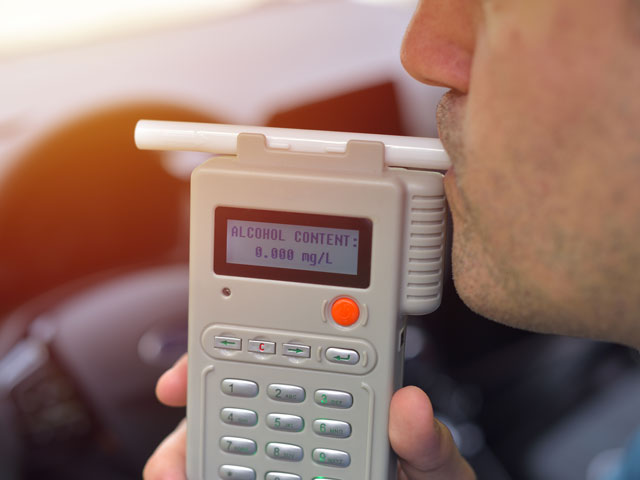 A man blowing into a breathalyzer to determine his BAC which is a direct result of the consumption of alcohol