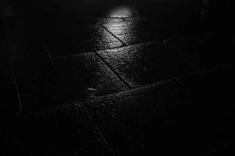 Light reflecting on wet stone tiles in black and white at night.