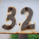 Brass letter box numbers bolted to a rusted white painted letterbox with even rustier bolts. The street number is thirty two.