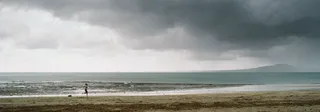 Panorama of a woman running up the beach with a cloudy mountain in the background