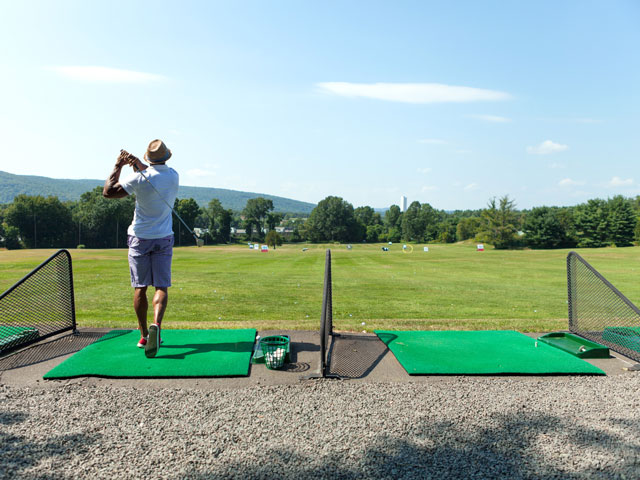 A golfer at a driving range teeing off with his driver from a tee box