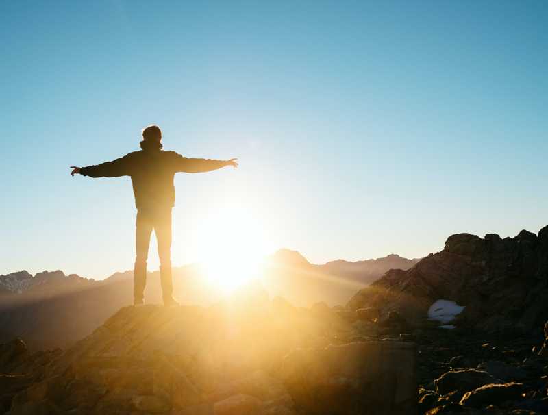 man standing watching sunrise behind mountain
