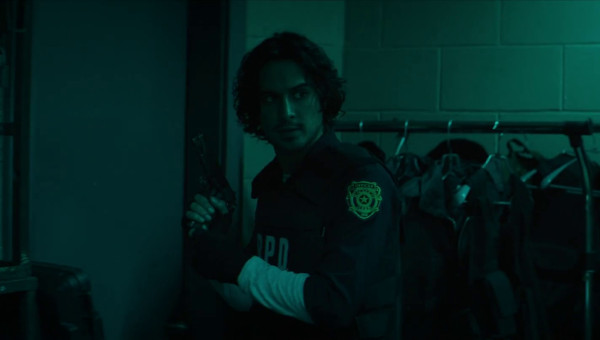 A still from Resident Evil: Welcome to Racoon City showing Leon bathed in teal light, now wearing his customary Resident Evil 2 RPD uniform and bullet proof-vest. He is holding a pistol and looking back over his shoulder at Claire, who is off camera.