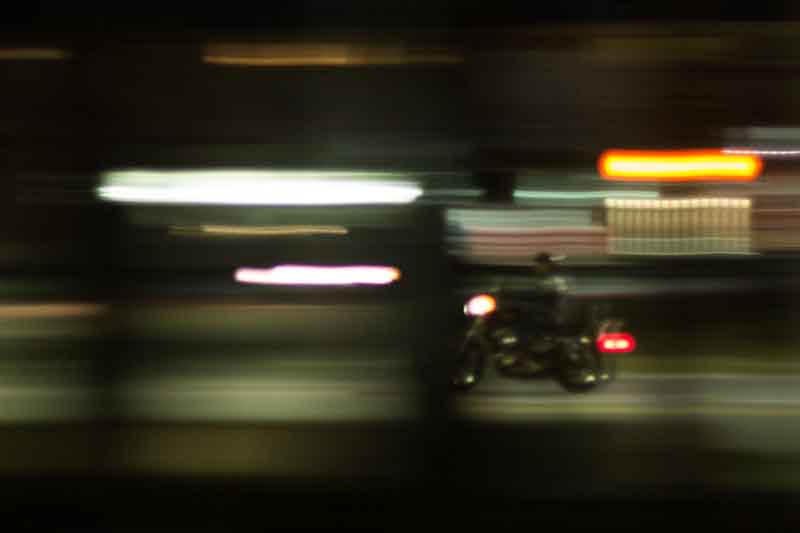 Blurry shot from behind some objects with a a motorcycle in the distance at night.