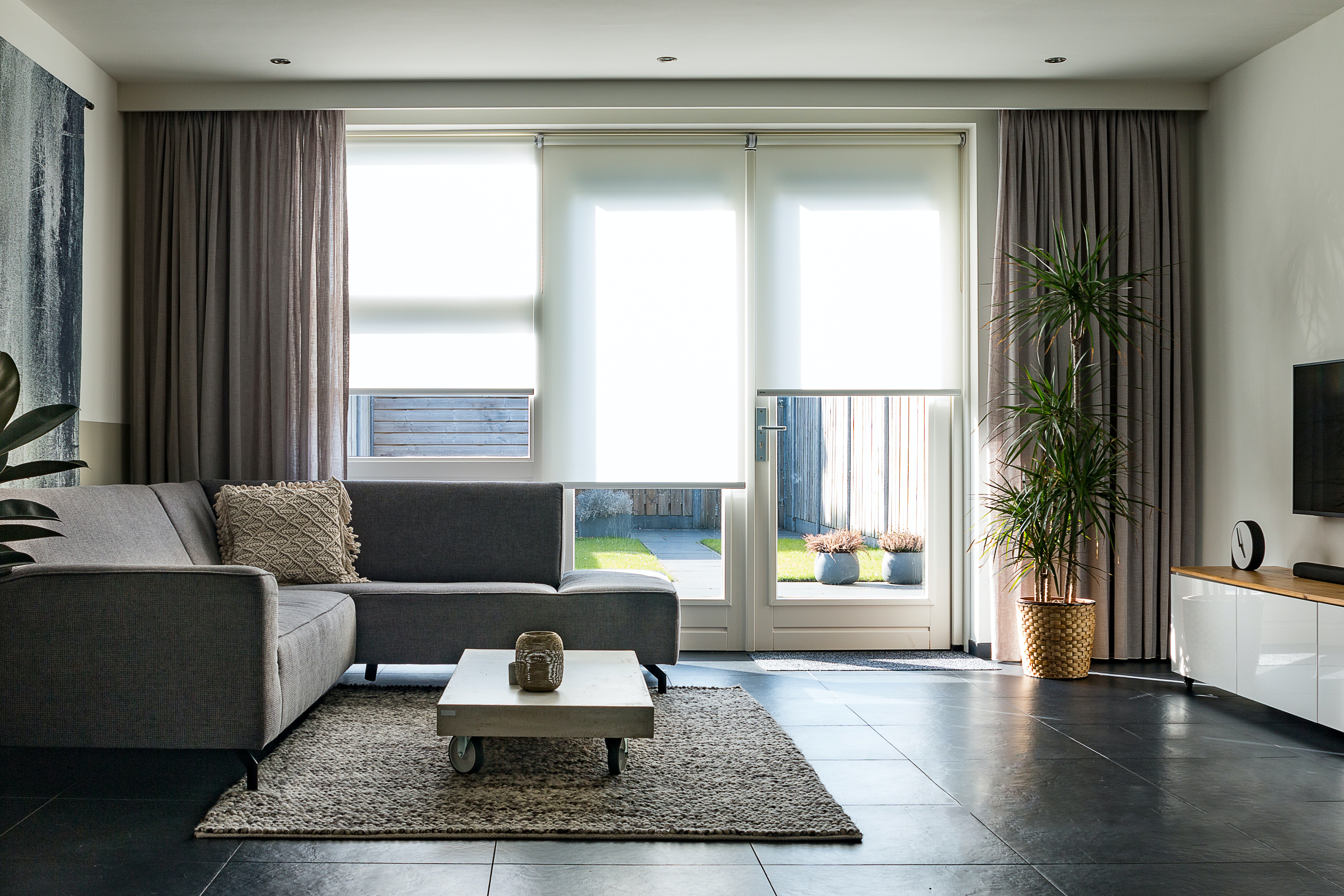 a living room with white shades and gray drapes