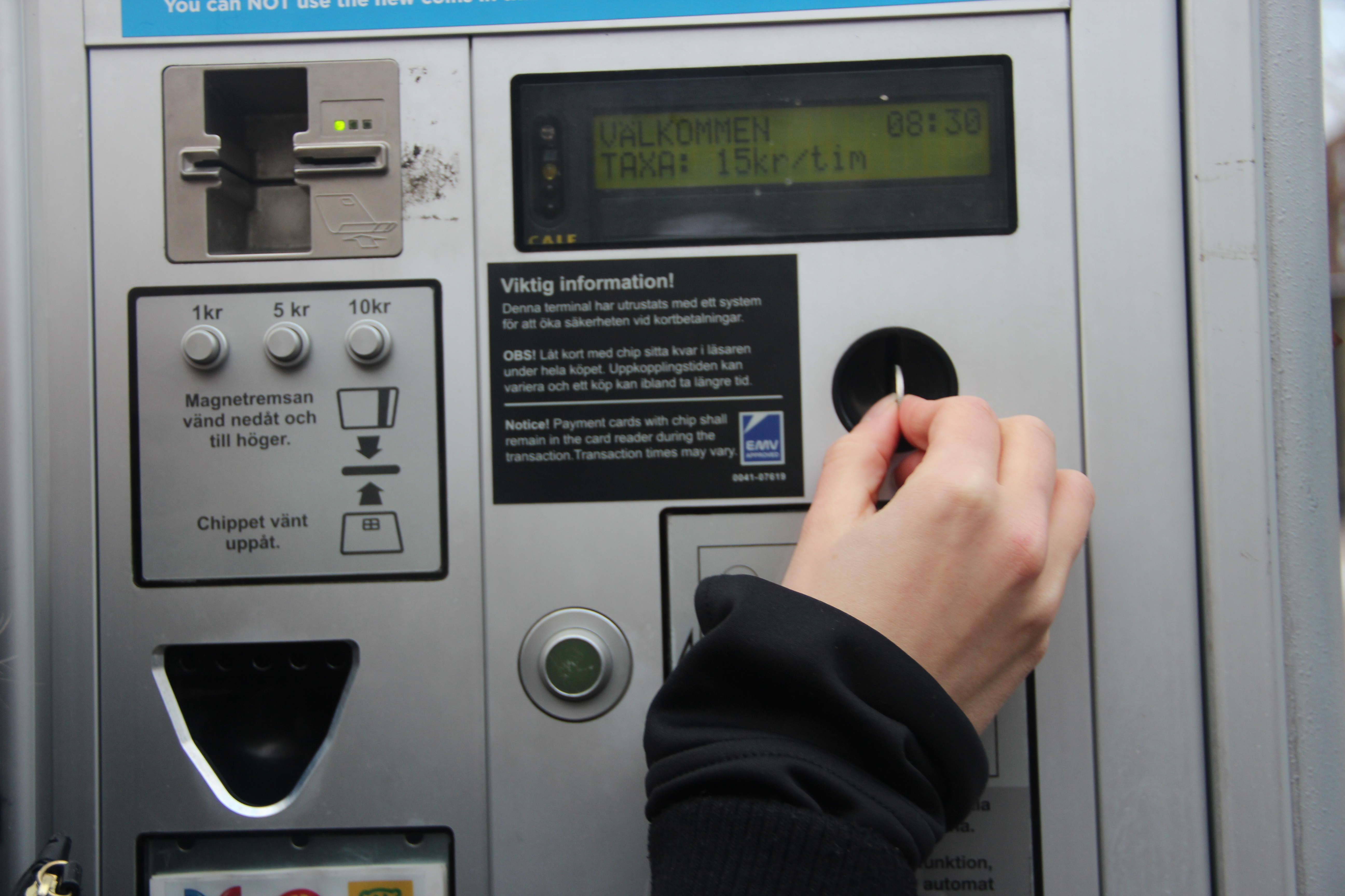 A hand inserting a coin into the parking meter to pay for a ticket